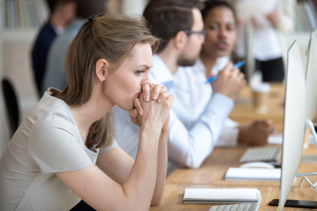 Upset frustrated and confused female worker folding hands on chin feels puzzled having problem troubles and doubts about business moments, sitting in shared modern office with multinational coworkers.