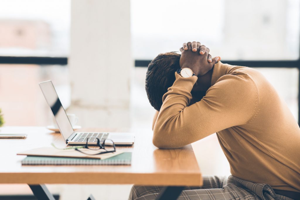 Problems At Work. Black businessman feeling upset and desperate, working at office, hands on head. Represents employee burnout.