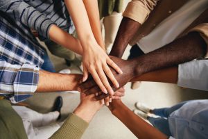 Cropped photo of multiracial people hands put on top of each other symbolizing unity. Represents cultural competence.