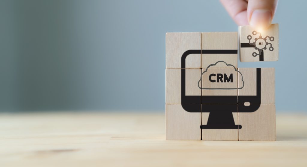 AI-CRM solution concept. Data driven marketing strategy with AI. For marketing plan, providing automated interaction to customer. Hand hold wooden cubes with AI-CRM icon on grey background, copy space.