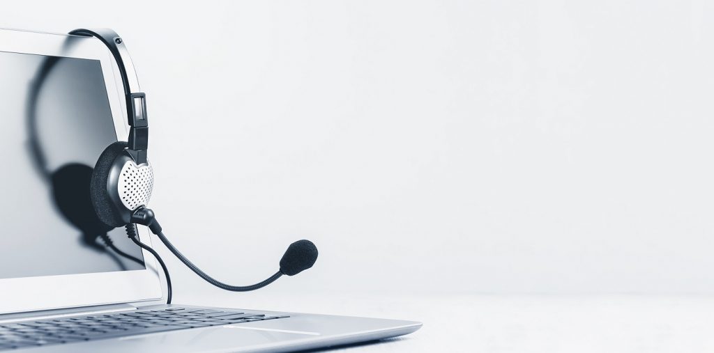 Laptop on a grey background with a headphones hanging on it.