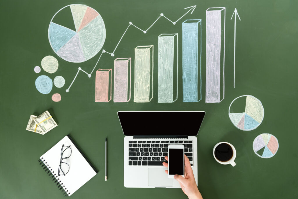 Top view of business person using digital devices at workplace with colorful graphs.