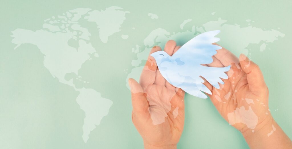 A hand holding a paper dove with the world map in the background.