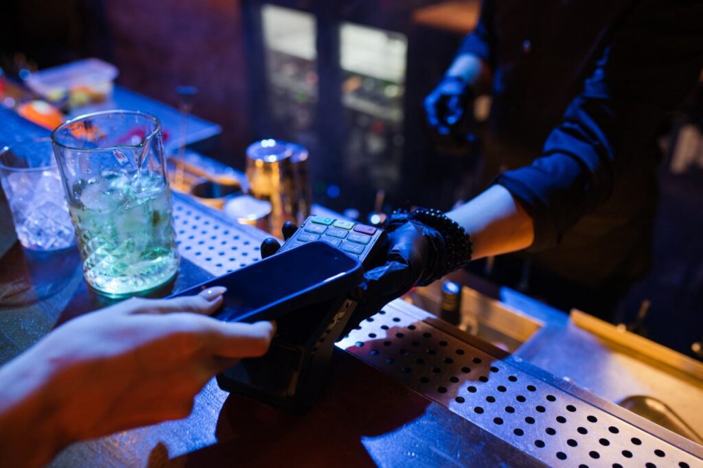 Woman paying for cocktails in the bar by mobile phone.