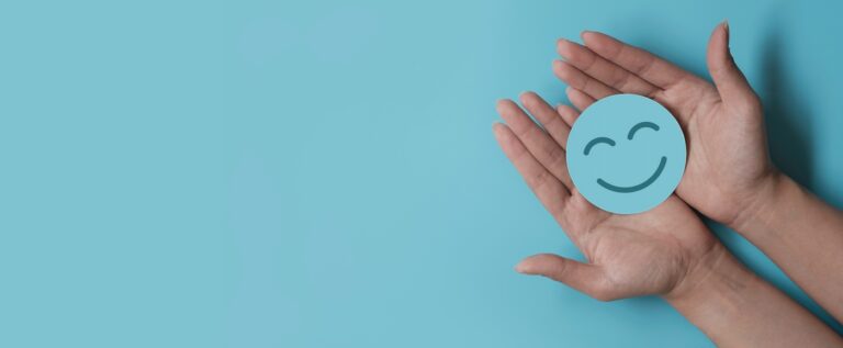 Upturned hands holding a blue smiley face over a matching blue background.