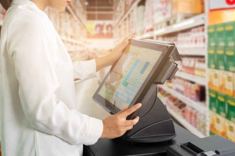 Cropped shot of female cashier staff standing and working with POS or point of sale machine at counter in supermarket.