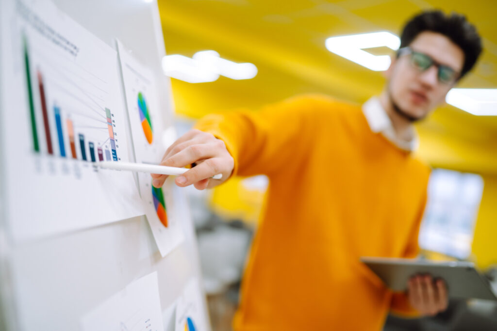 A picture of a man in an orange shirt presenting a set of bar graphs.