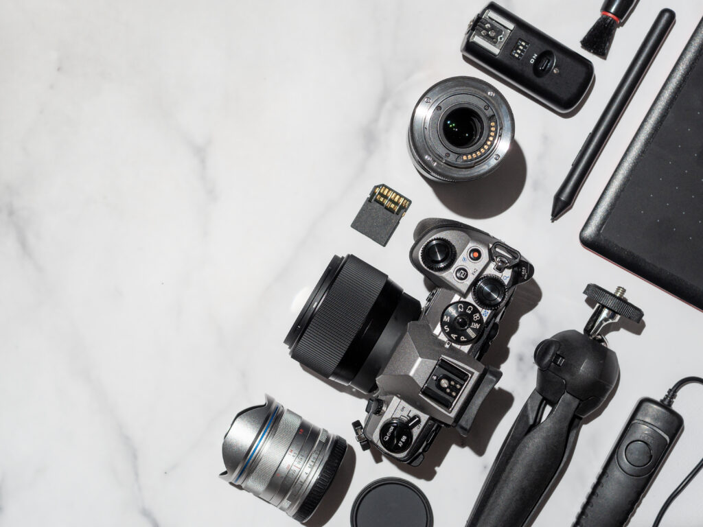 Photographer workplace with dslr camera, lens, pen tablet and camera accessories on white marble background. Camera, photography, visual content concept. Flat lay or top view. Copy space. Hard light.