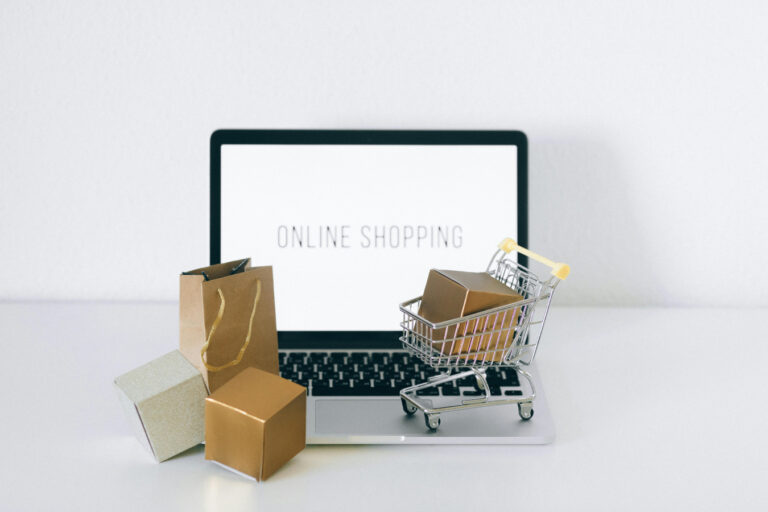 Online shopping on laptop with mini push cart and boxes.