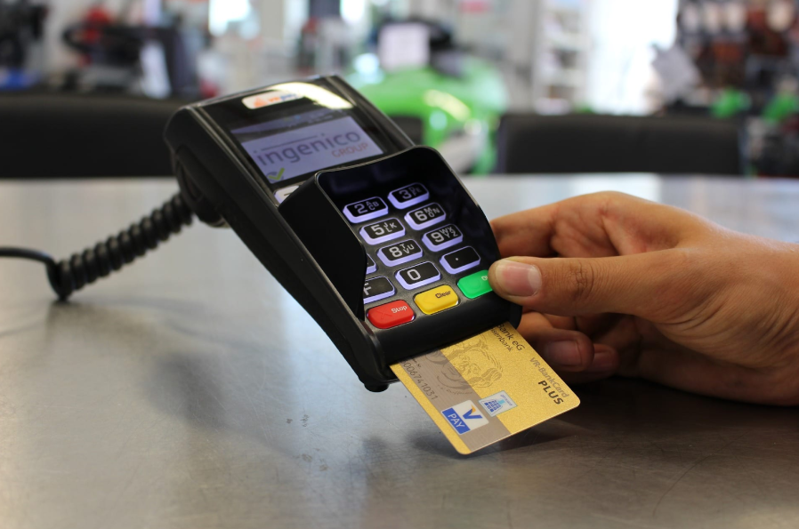 Hand inserting a gold chip card into an Ingenico payment terminal on a countertop