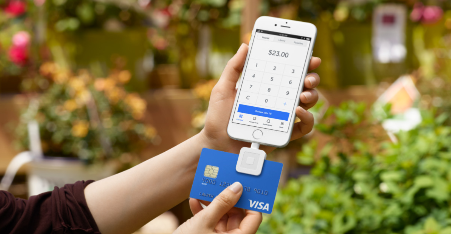 Person swiping a blue Visa card through a Square reader attached to an iPhone showing a $23 charge