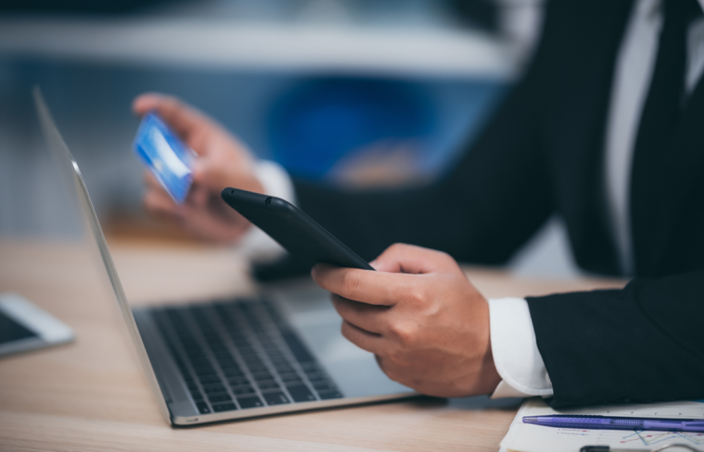 Businessman making an online payment using a smartphone, credit card, and laptop