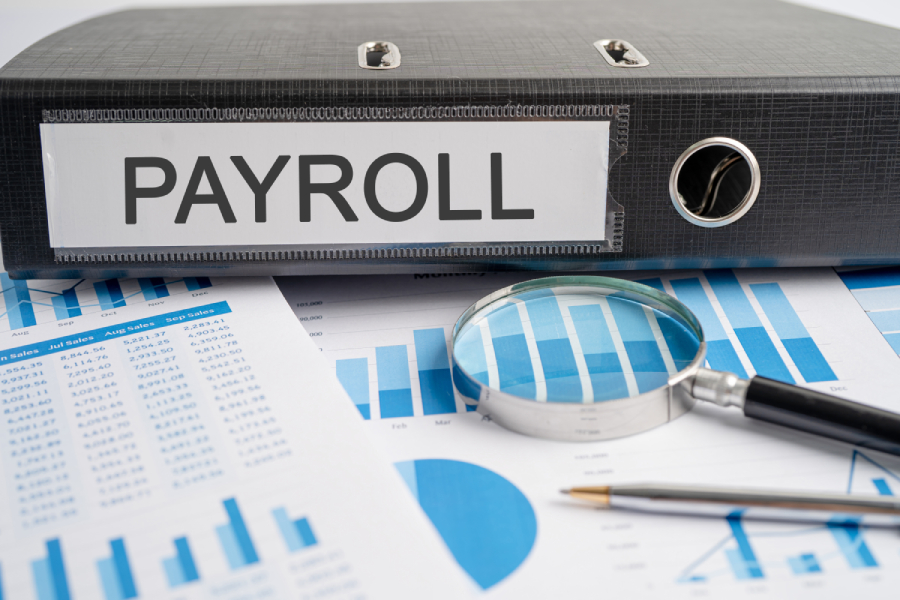 Employee payroll on binder and audit reports with magnifying glass.