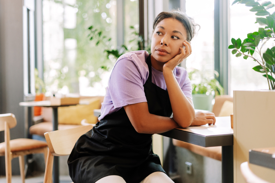 Tired waitress leaning on a table in a coffee shop looking away pensively.