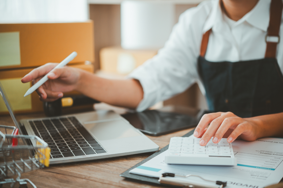 A business owner computing expenses and payments on laptop using a calculator.