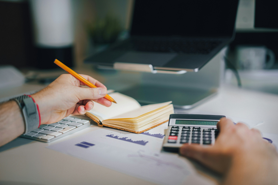A person doing accounting works with a pencil, notebook, and calculator.