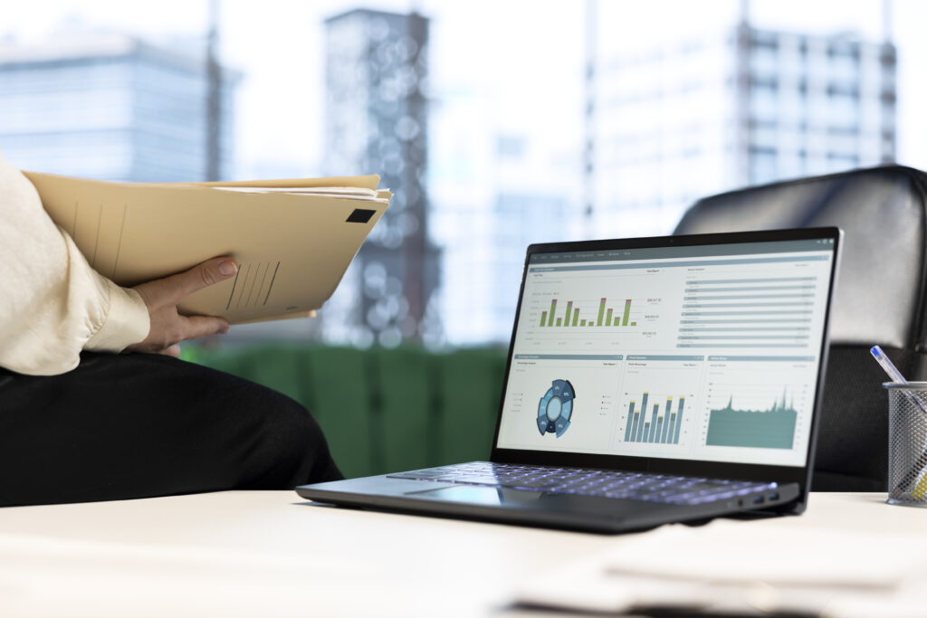 Financial reporting software dashboard displaying bar charts and analytics data on a laptop in a modern office setup.