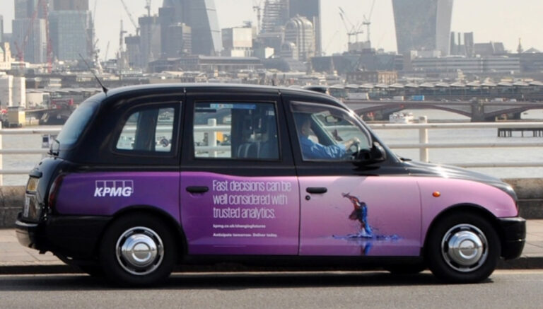 Black London taxi wrapped in a purple KPMG advertisement beside the River Thames and city skyline.