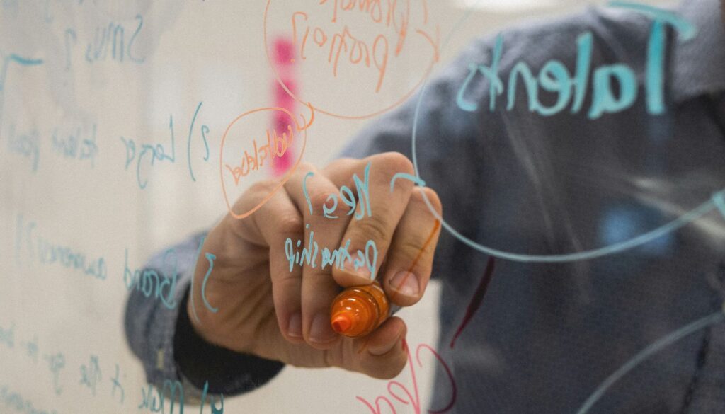 person writing on a glass whiteboard